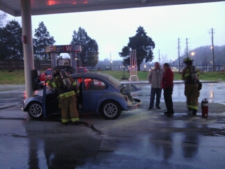 Jim Wilson of the Y-12 Fire Department used a fire extinguisher to put out the fire in the back of a Volkswagen Beetle at Weigel's gas station and convenience store on South Illinois Avenue on Saturday evening, Dec. 24, 2016. Also pictured above are Eric Mocsari of the Oak Ridge Fire Department, left, and ORFD Battalion Chief Eric Rackard, second from right. (Photo by John Huotari/Oak Ridge Today)